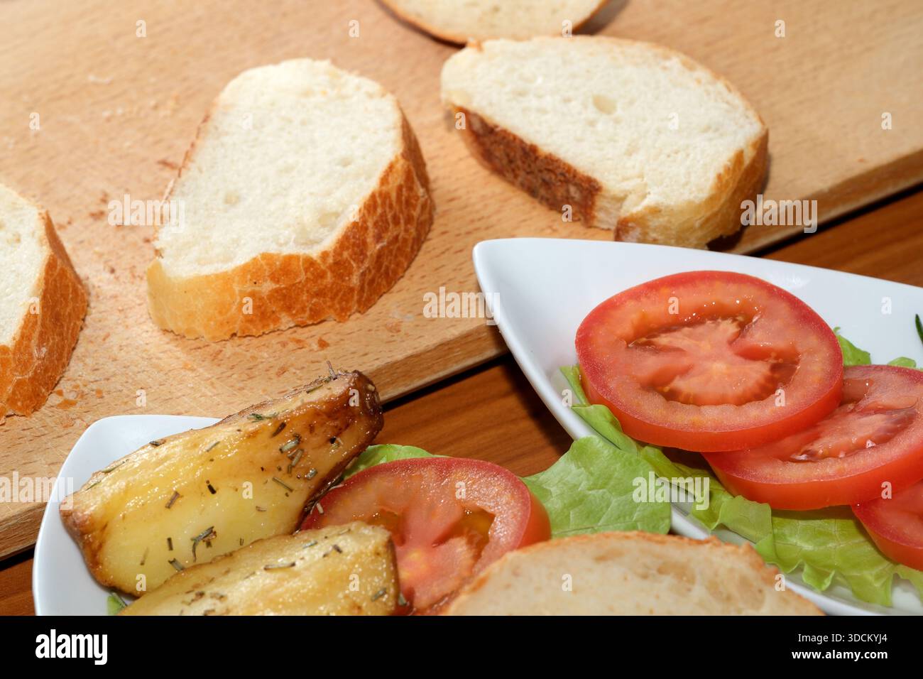 Knusprige Brotscheiben begleiten frische Tomaten und Gemüse auf einem Holztisch. Stockfoto