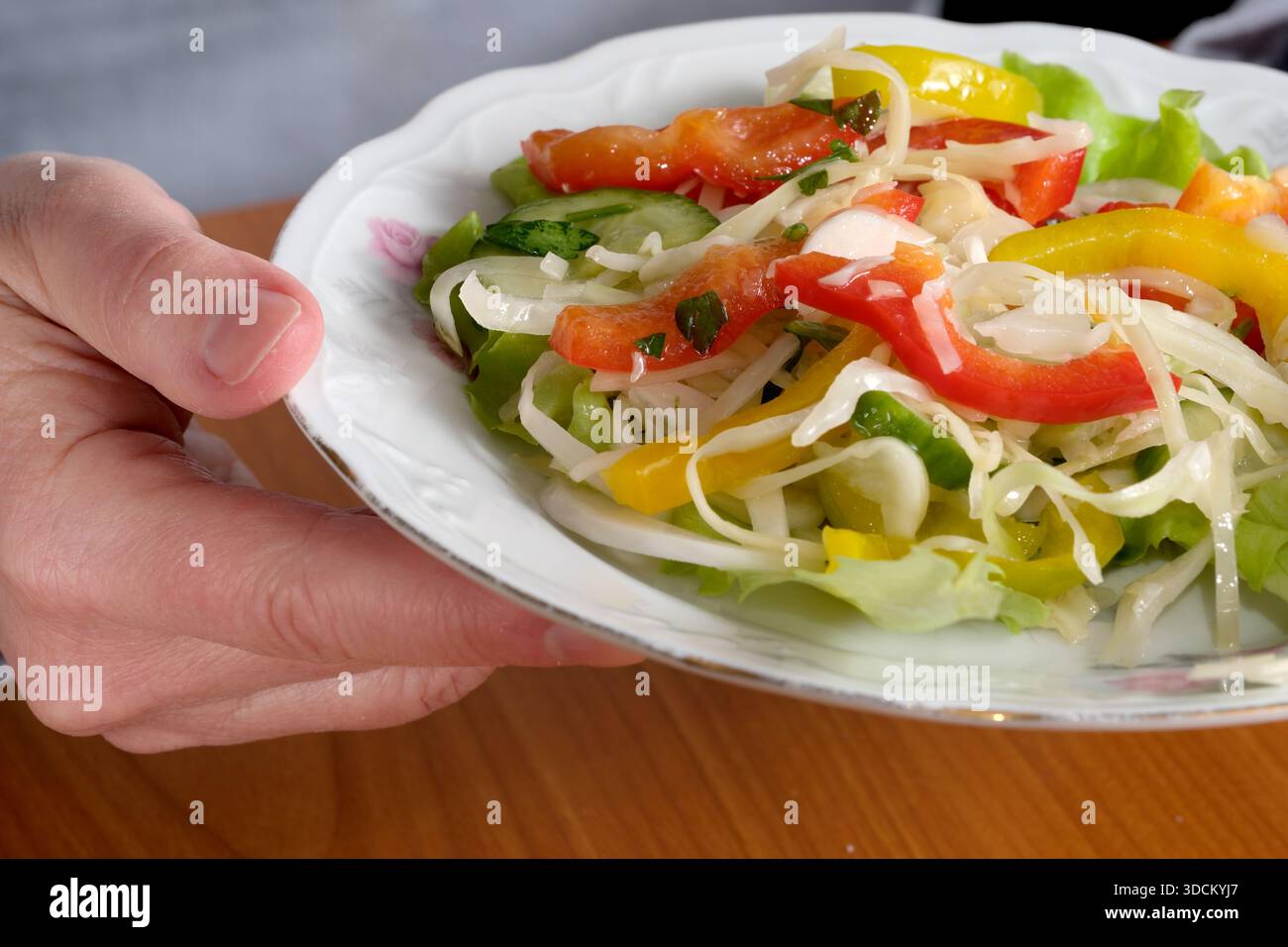 Eine Hand präsentiert einen farbenfrohen Salat mit knusprigem Gemüse und lebhaften Farben, die einen Geschmack einladen. Stockfoto