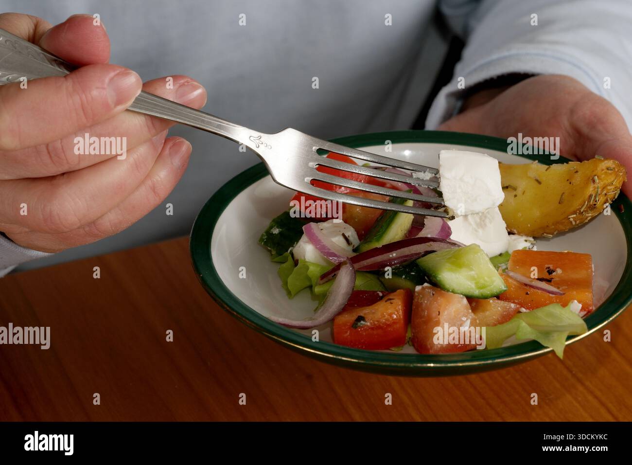 Eine Hand hält vorsichtig eine Gabel voller lebendiger Salatzutaten, die zum Verzehr bereit sind. Stockfoto