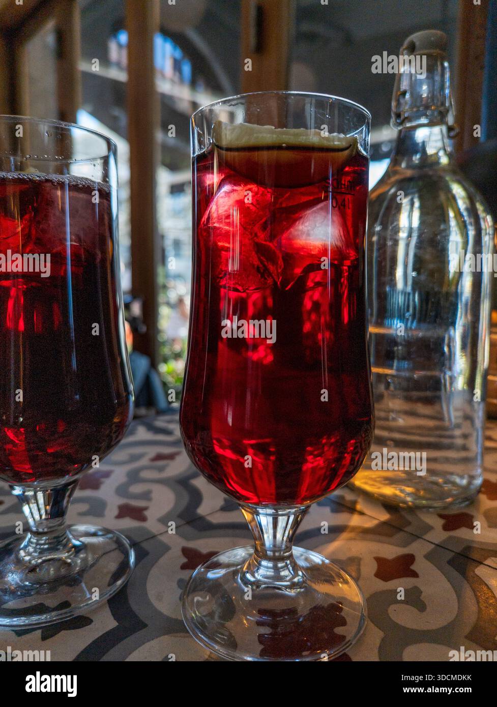Erfrischendes Getränk aus roter Preiselbeere mit Eis und Zitrone in einem hohen Glas auf einem gemusterten Tisch Stockfoto