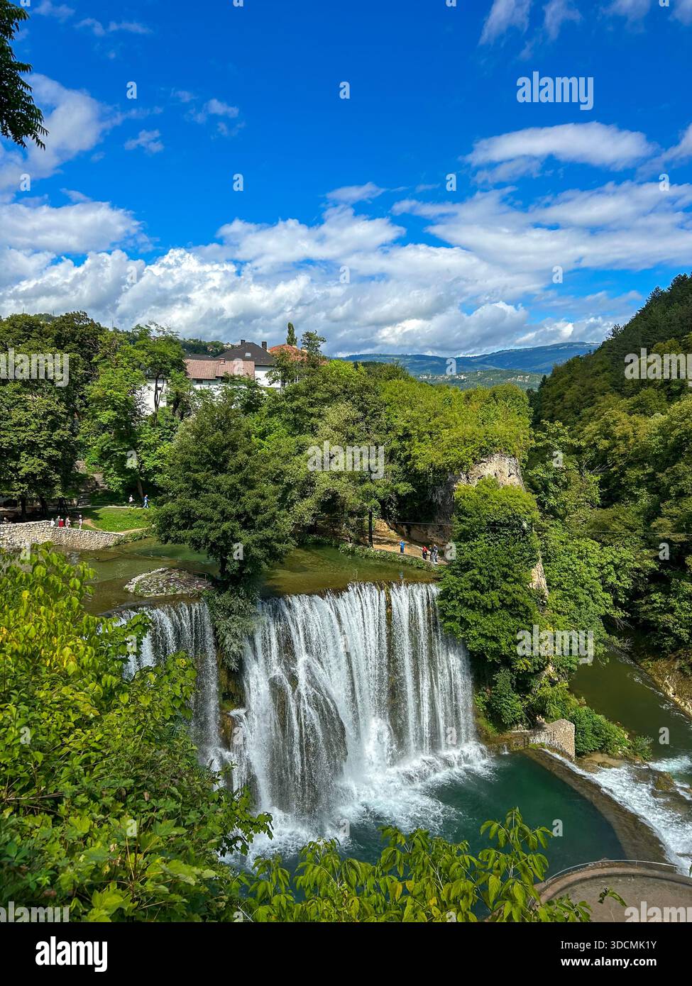 Ein atemberaubender Blick auf den Jajce Wasserfall, umgeben von üppigem Grün und einem klaren blauen Himmel, der die natürliche Schönheit von Bosnien und Herzegowina zeigt. - Smartphone-aufgenommenes Stockfoto