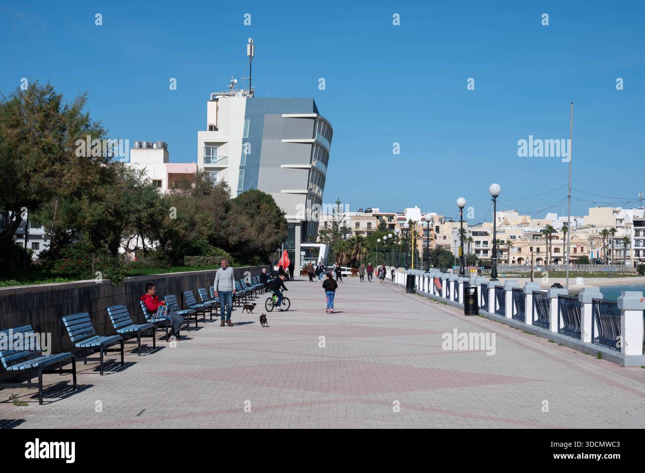 Pier am Strand von BirÅ¼ebbuÄa mit wenigen Einheimischen, die die ruhige Wintersonne genießen, schafft eine ruhige Urlaubsatmosphäre außerhalb der Touristensaison BirÅ¼ebbuÄa, Malta, 6. Dezember 2025 Stockfoto