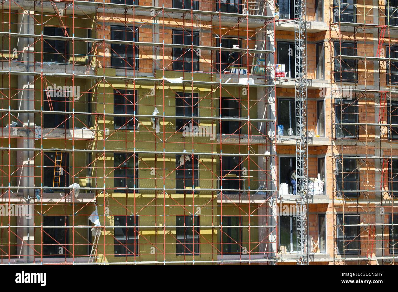Im Bau befindliches Wohnhaus mit umfangreichem Gerüst, freiliegendem Mauerwerk, Dämmschichten und installierten Fenstern. Stockfoto
