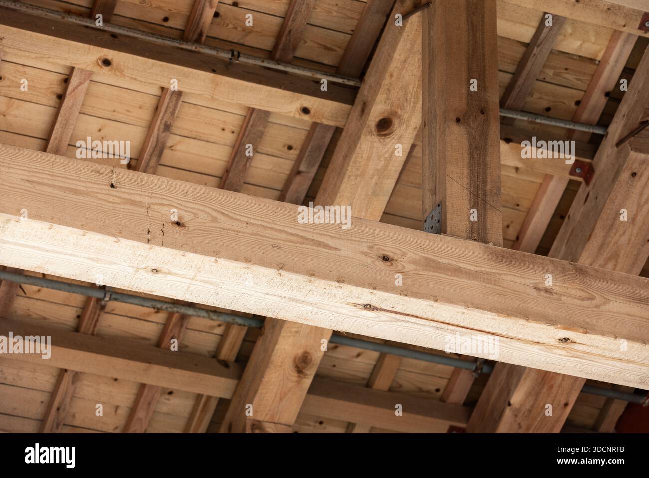Ein Blick aus der Nähe auf schwere Holzbalken und Dachrahmen in einem Gebäude im Bau. Warme Holztöne, Metallklammern und sichtbare Fugen bringen das Handwerk zum Ausdruck Stockfoto