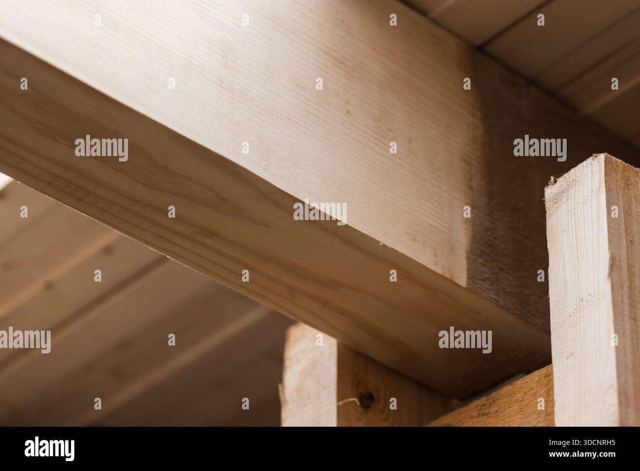 Warme, naturbelassene Holzbauszene mit sich kreuzenden Balken und stabilen Fugen. Ideal für Tischlerei-, Rahmen-, Renovierungs- und Bauthemen Stockfoto