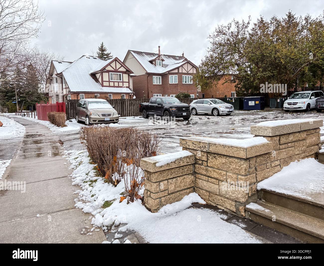 Eine Wohnstraße und ein Parkplatz in Kanada, bedeckt mit matschigem Schnee nach einem leichten Wintersturm. Häuser mit schneebedeckten Dächern und geparkten Autos sind vorhanden Stockfoto