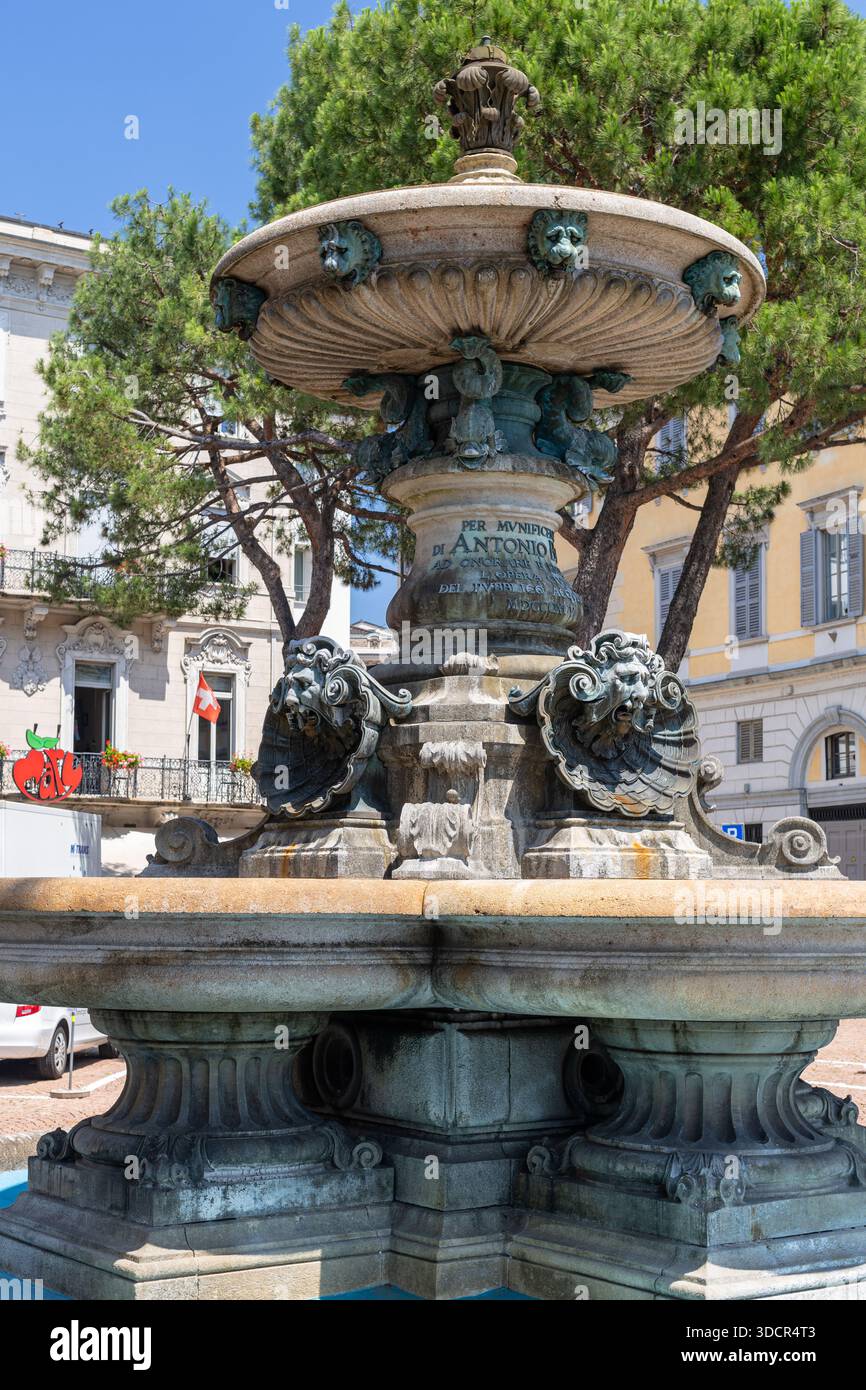 Ein großer Steinbrunnen mit geschnitzten Löwen und verzierten Basreliefs auf einem europäischen Stadtplatz mit farbenfrohen modernen Gebäuden im Hintergrund Stockfoto