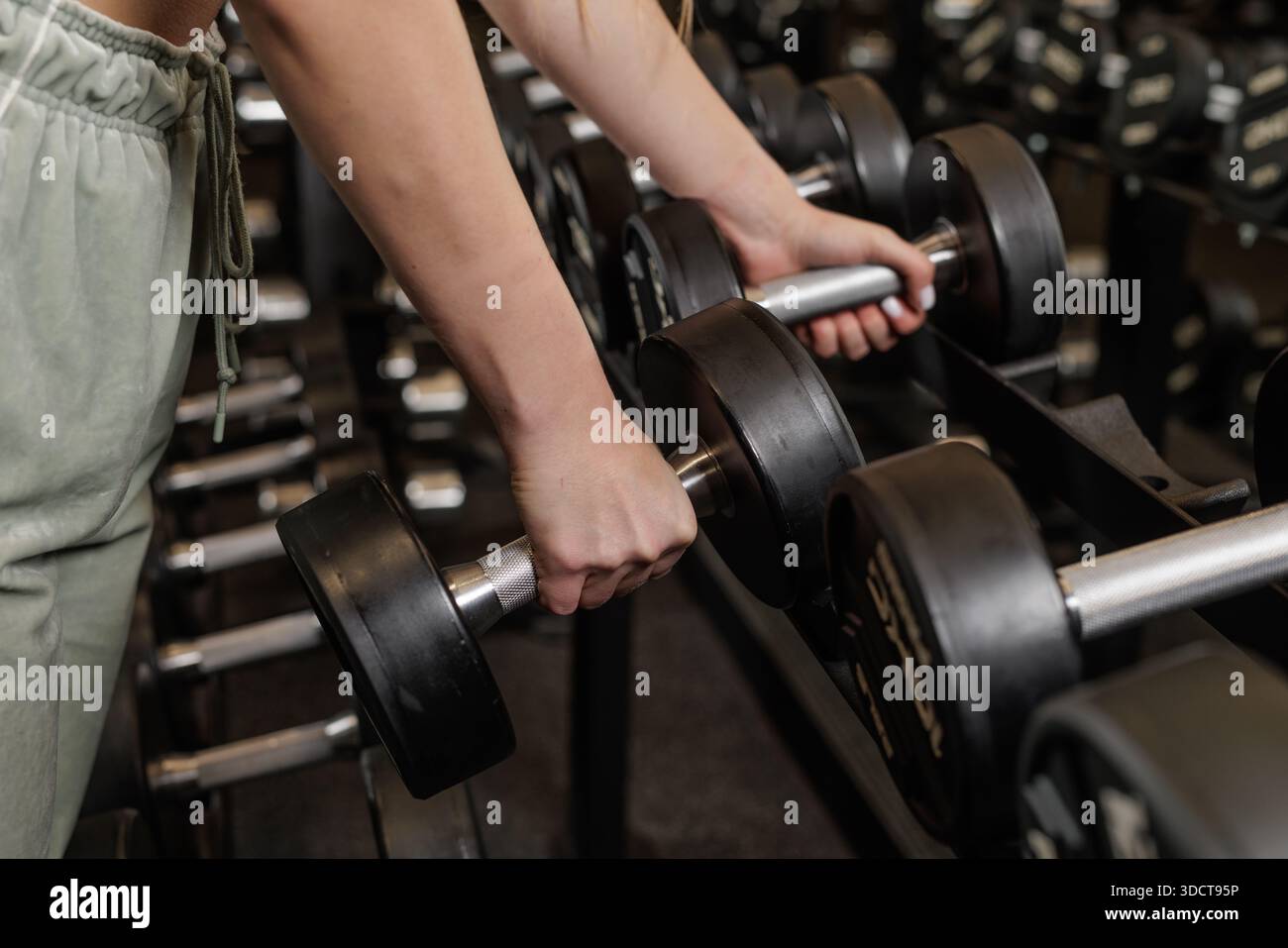 Nahaufnahme von Frauenhänden, die die Hantel im Fitnessclub vom Rack nehmen und sich auf das Gewichtheben vorbereiten Stockfoto