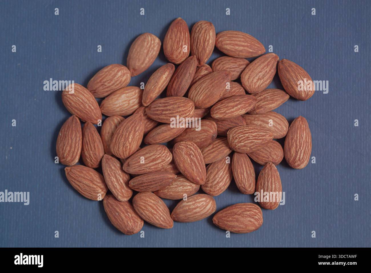 Mandeln liegen auf einem einfachen Blatt Papier auf und betonen ihre natürliche Textur in einer sauberen minimalen Szene. Stockfoto