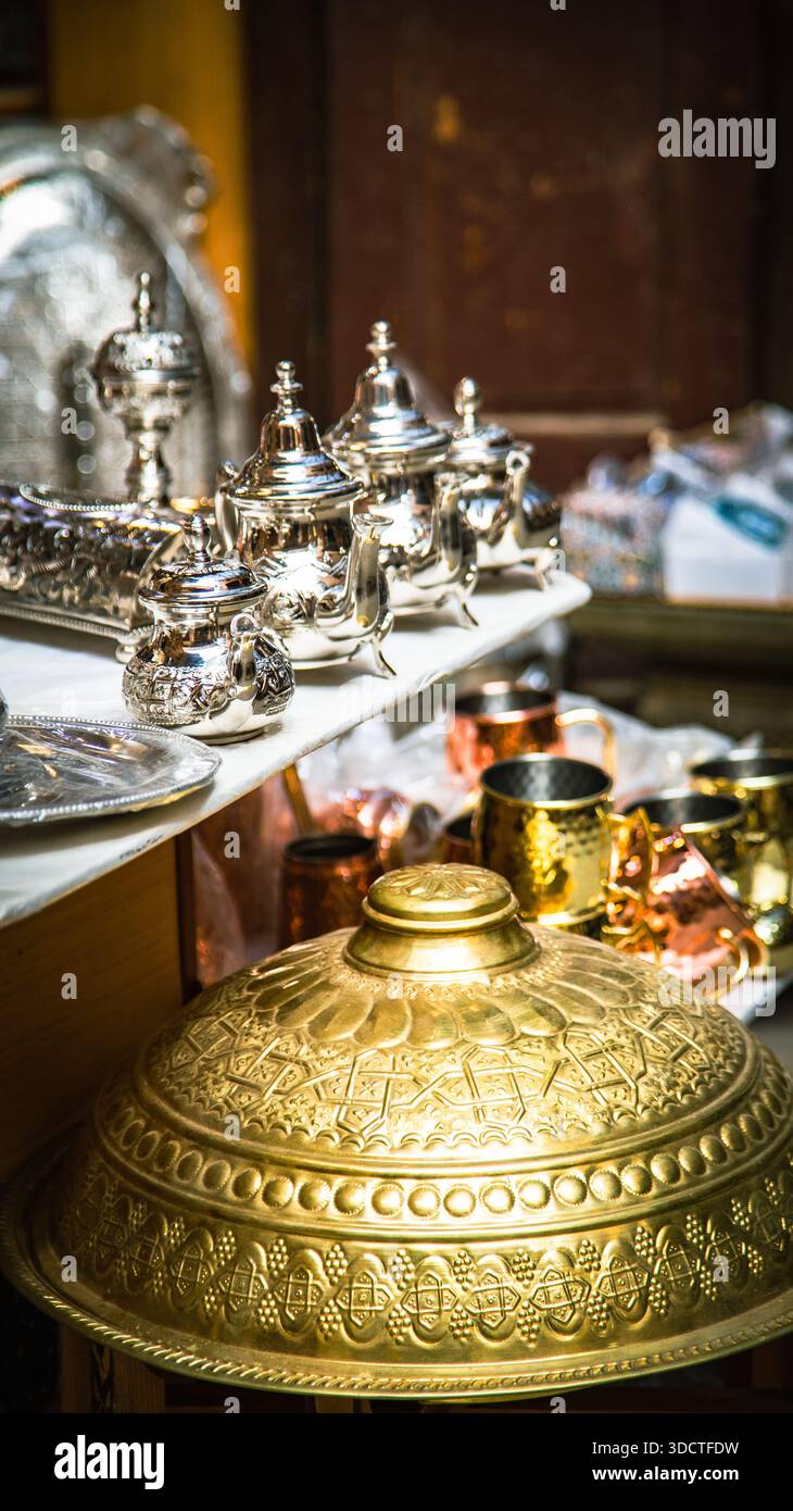 Marokkanische Handwerkskunst in Fès: Fein gravierte silberne Teekannen, Tabletts, goldene Deckel und kupferne Becher in einem traditionellen Geschäft. Stockfoto
