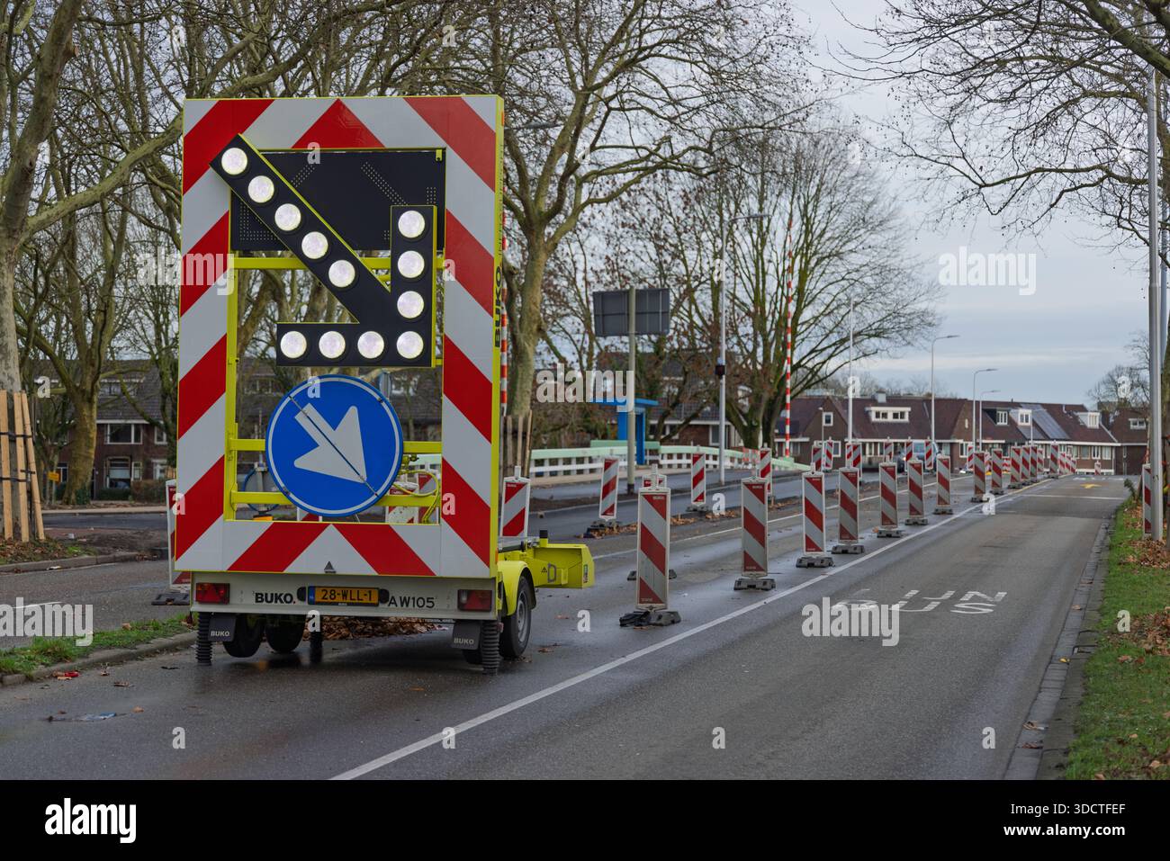 Großer mobiler LED-Trailer mit Verkehrspfeilen auf nasser Straße mit Kegeln, die den Verkehr bei Straßeninstandhaltungsarbeiten in den Niederlanden lenken. Stockfoto