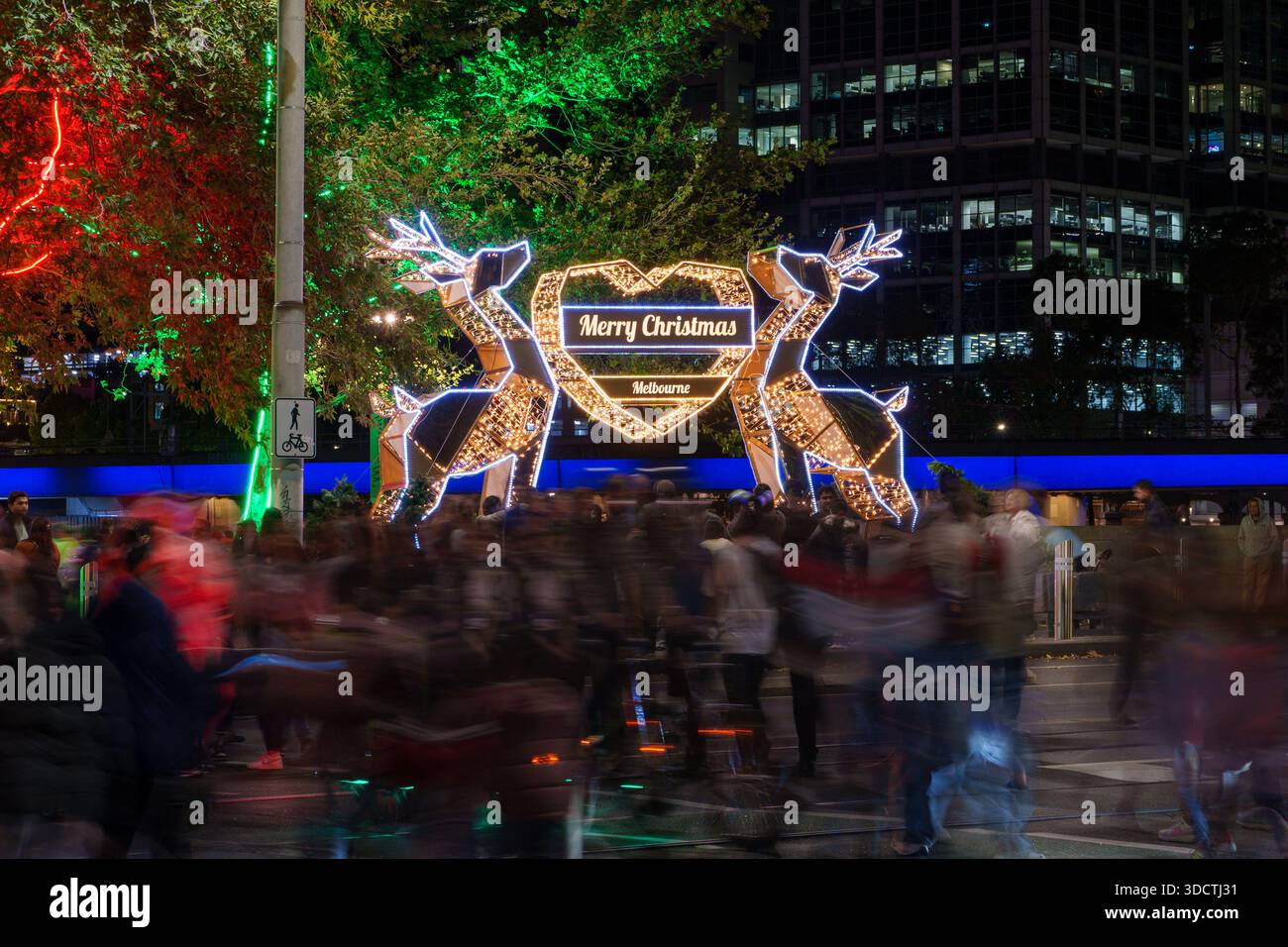 Bei einer Langzeitbelichtung werden unscharfe Menschen gefangen, die nachts in Melbourne ein fröhliches Rentierlicht bewundern. Stockfoto