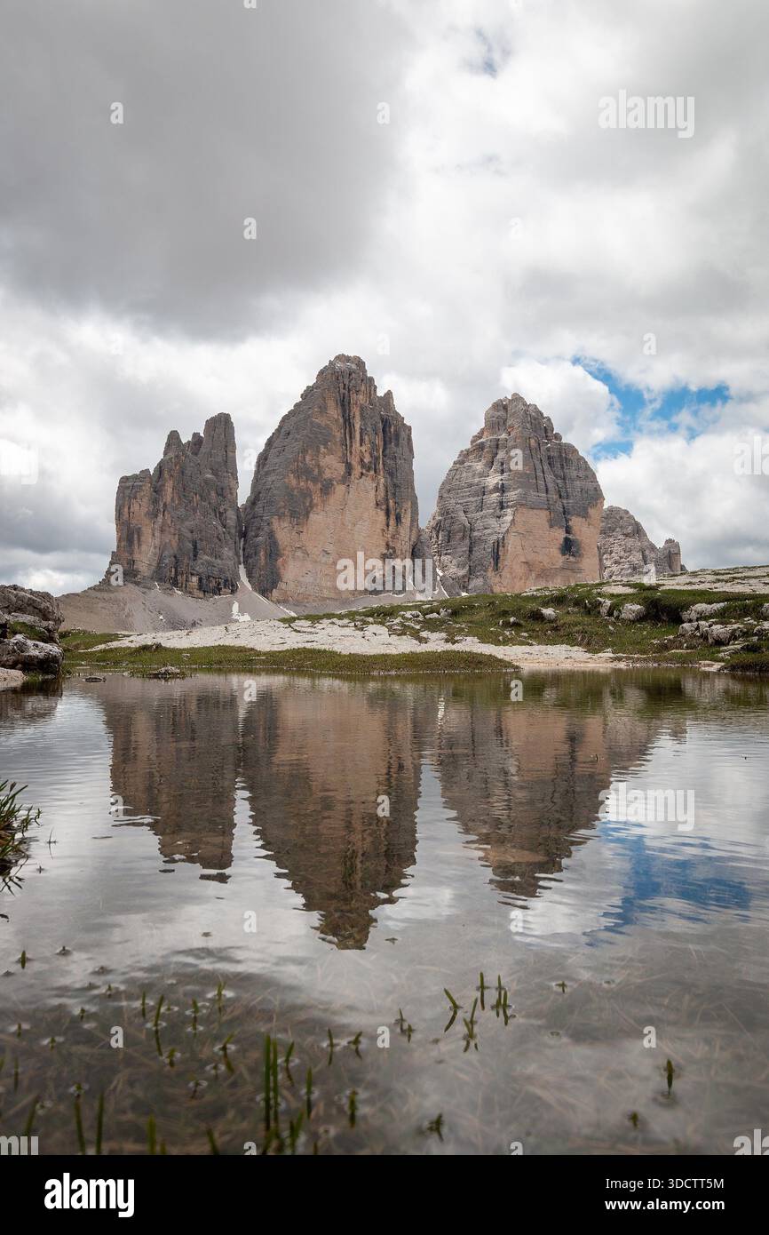 Niedriger Blickwinkel auf Tre Cime di Lavaredo in einer Pfütze; Cima Grande, Cima Ovest und Cima Piccola über hellem Kalksteingeröll vor blauem Himmel mit Wolken Stockfoto