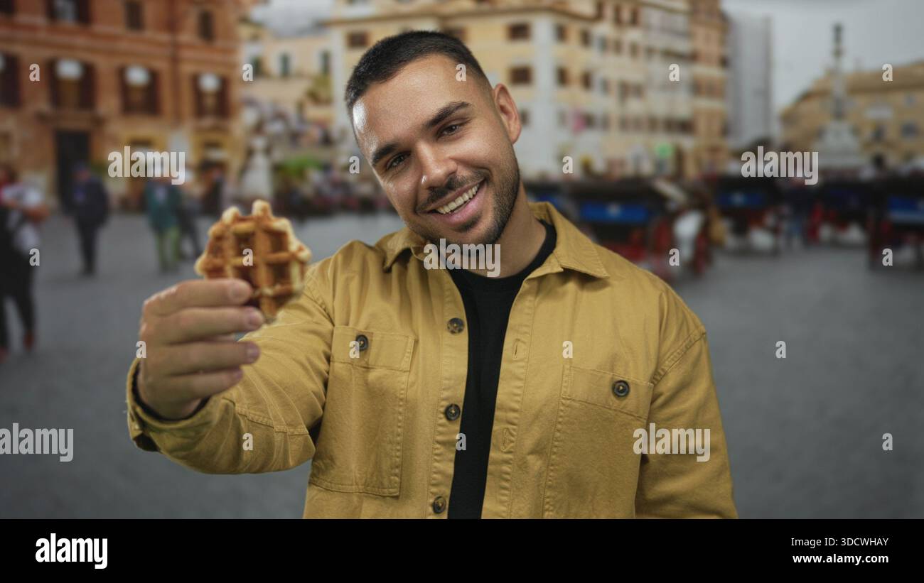 Junger Mann mit Waffeln und Lächeln, während er ein Gebäck in einer überfüllten Straße der Stadt probiert; kulinarische Köstlichkeiten. Stockfoto