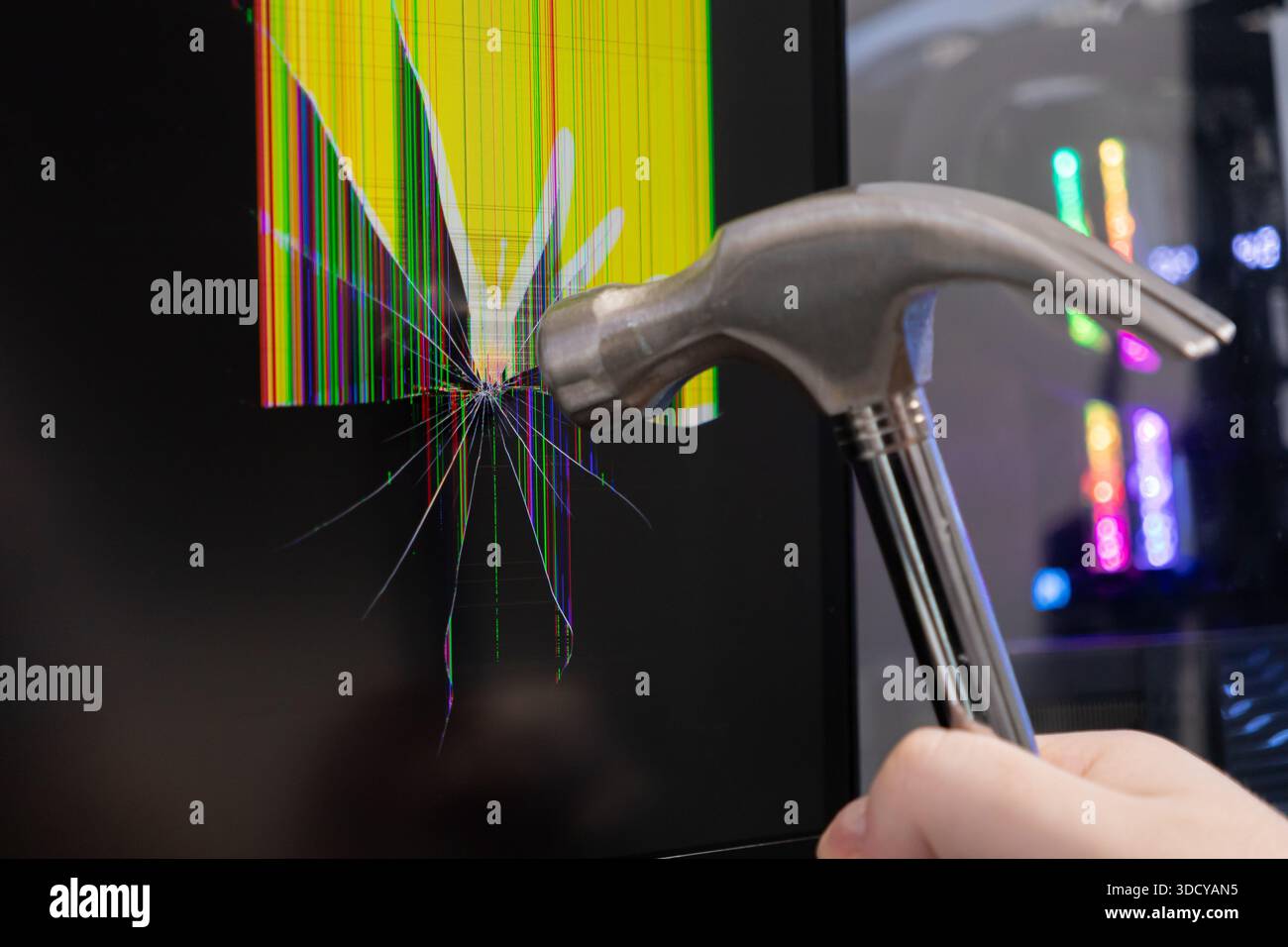 Nahaufnahme einer Hand, die einen Hammer hält und auf ein Display einwirkt, was zu schweren Bildschirmschäden, bunten Pixelverzerrungen und einem kritischen Systemausfall führt Stockfoto