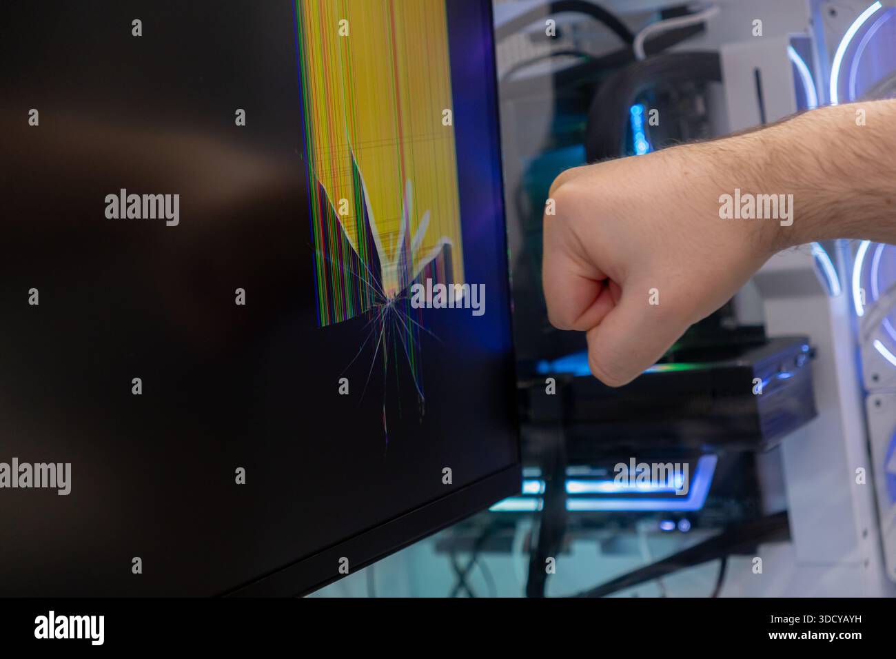 Die geschlossene Faust einer Person in der Nähe eines beschädigten Computermonitors, der einen stark gerissenen Bildschirm mit bunten toten Pixeln zeigt, die technica symbolisieren Stockfoto