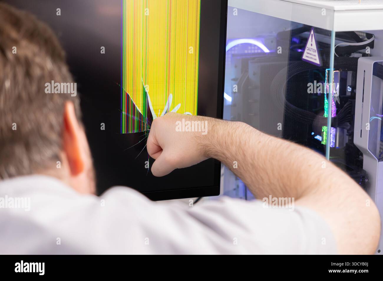 Nahaufnahme einer wütenden Person, die einen Computermonitor zerschmettert, mit einem zertrümmerten Display mit verzerrten gelben und bunten Pixeln, die Graben symbolisieren Stockfoto