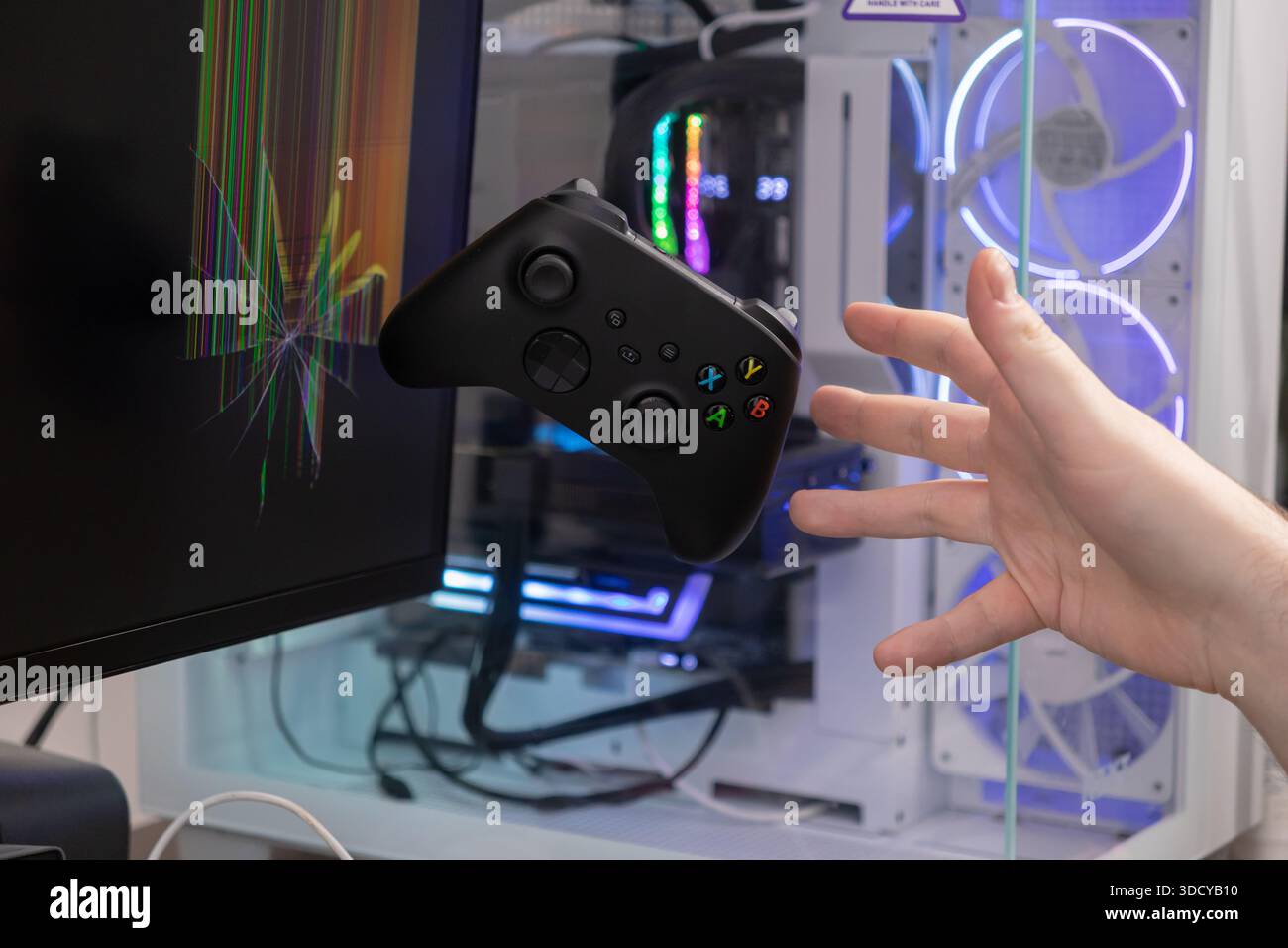 Ein schwarzer Gamecontroller schwimmt mitten in der Luft, während eine Hand auf ihn zugreift, im Kontrast zu einem zertrümmerten Monitor und einem Gaming-PC, der Spielfrustratio zum Ausdruck bringt Stockfoto
