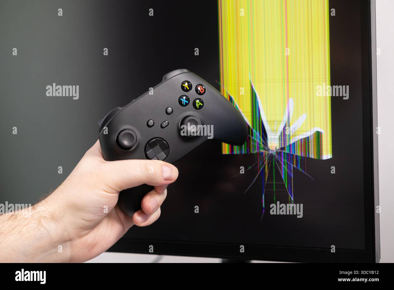 Nahaufnahme einer Hand, die einen modernen schwarzen Video-Game-Controller hält, positioniert vor einem stark zerrissenen Monitor, der eine farbenfrohe digitale da anzeigt Stockfoto