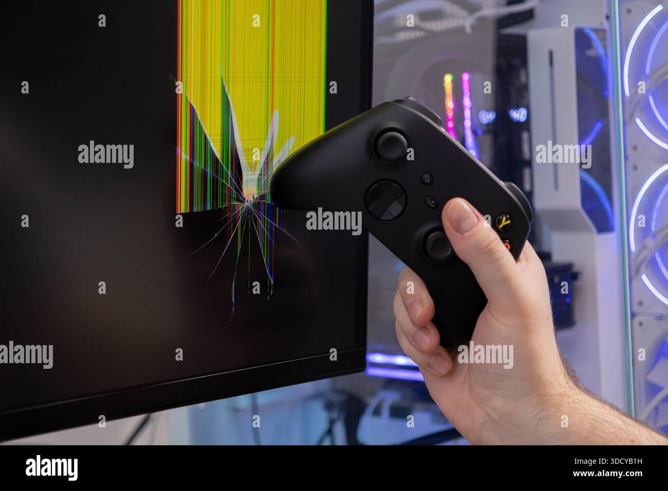 Nahaufnahme einer Hand, die einen schwarzen Videospiel-Controller fest packt und auf einen Monitor gerichtet ist, der einen stark zerschmetterten Bildschirm mit bunten Linien zeigt Stockfoto