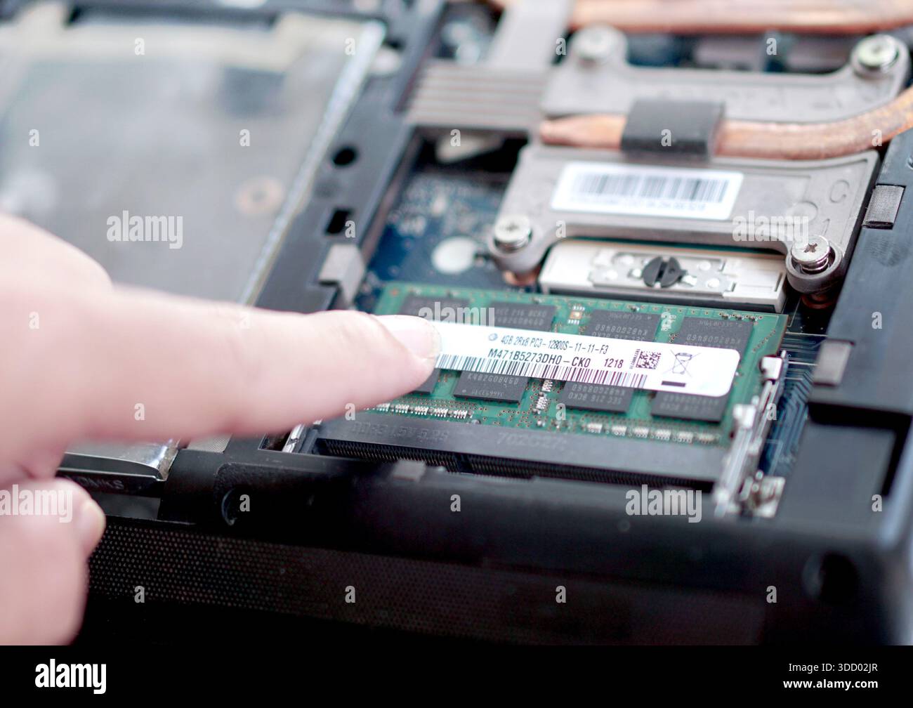 Ein Benutzer, der speziell auf die Modellnummer auf einem Laptop-RAM-Stick-Etikett zeigt, um die Kompatibilität für ein System-Upgrade zu identifizieren. Stockfoto