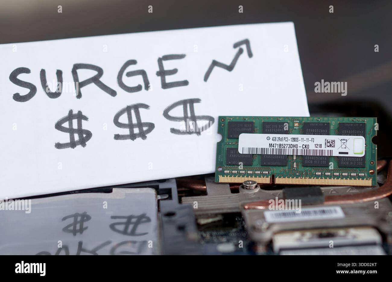 Ein Laptop-RAM-Modul neben einem „ÜBERSPANNUNGSSCHILD“ mit Dollarsymbolen und einem Aufwärtspfeil. Zeigt steigende Komponentenkosten und Inflation im tec Stockfoto