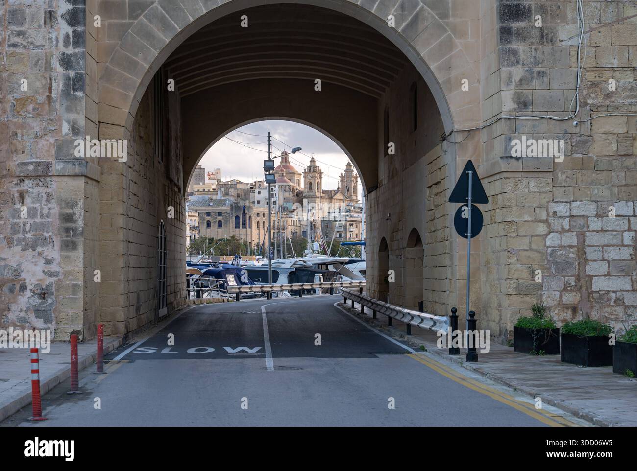 Blick durch einen monumentalen Tunnelbogen, der den Hafen von Birgu umrahmt, mit Booten und historischen Gebäuden, die den maltesischen architektonischen und maritimen Charme von Birgu, Malta, 10. Dezember 2025 erfassen. Stockfoto