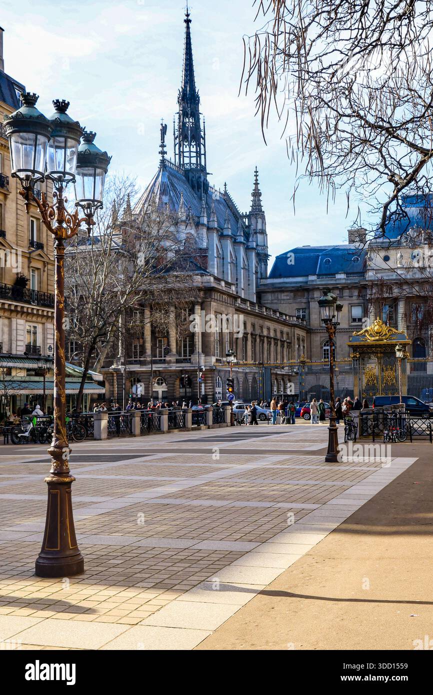 Paris. Der gotische Turm von Sainte-Chapelle erhebt sich über dem historischen Justizpalast in Paris, eingerahmt von kunstvollen Straßenlaternen auf einem sonnigen Stadtplatz. Stockfoto