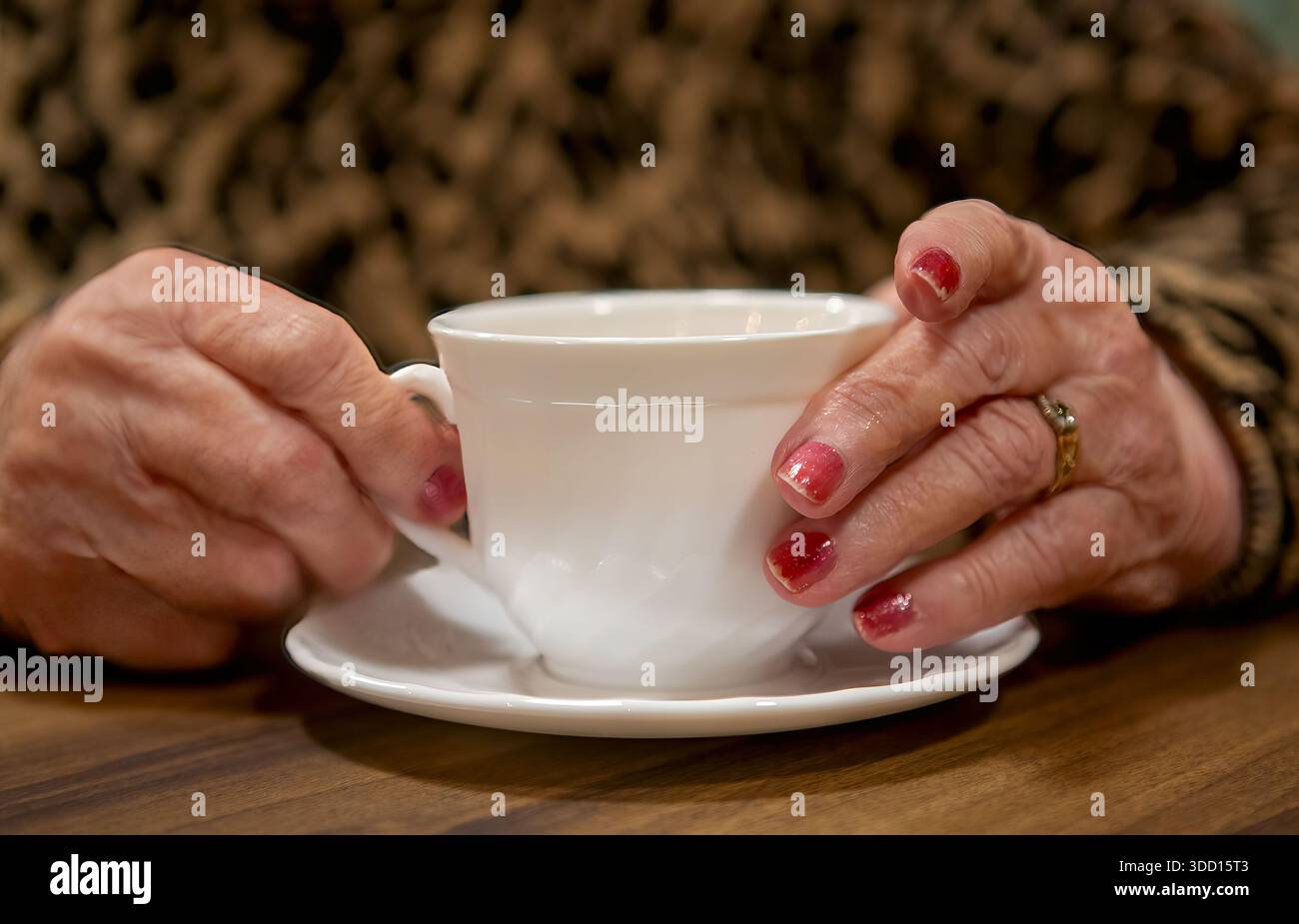 Die Hände einer älteren Frau halten eine Tasse Tee Stockfoto