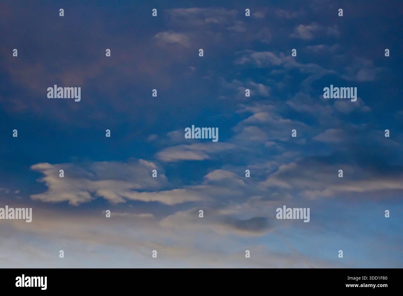 Blick in die Höhe eines dramatischen Abendhimmels mit tiefblauen und violetten Tönen mit weichen, nebeligen Wolken und subtilen Lichtverläufen. Stockfoto