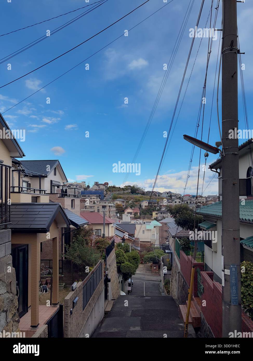 Kobe, Präfektur Hyogo, Japan. Enge Wohnstraße auf einem Hügel mit Freileitungen, Versorgungsmast und Nachbarhäusern. - Smartphone-aufgenommenes Stockfoto