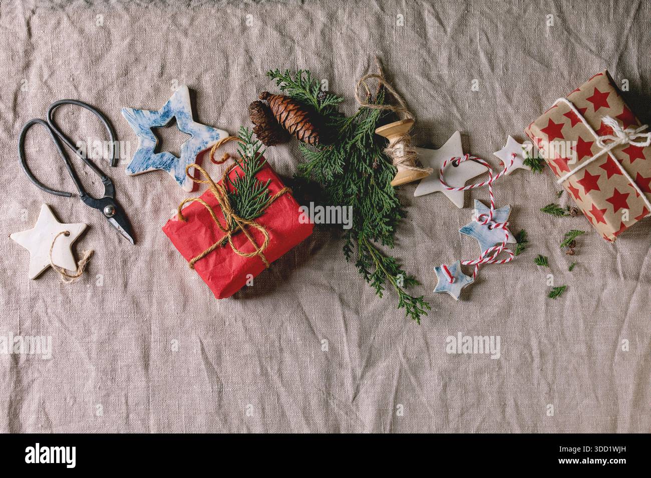 Weihnachtsdekoration Keramiksterne weiß und blau glasiert, verschiedene Größen, Geschenkboxen in Bastelpapier, grüne Zweige über Leinentuch als Hintergrund. Weihnachten, Neujahr Geschenkverpackung. Flach, Platz. Stockfoto