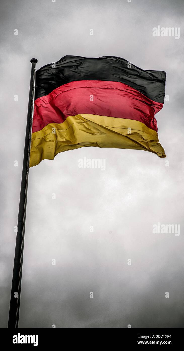 Deutsche Nationalflagge winkt auf Fahnenmast vor dramatisch bewölktem Himmel, minimale Komposition mit Kopierraum und patriotischem Konzept. Stockfoto