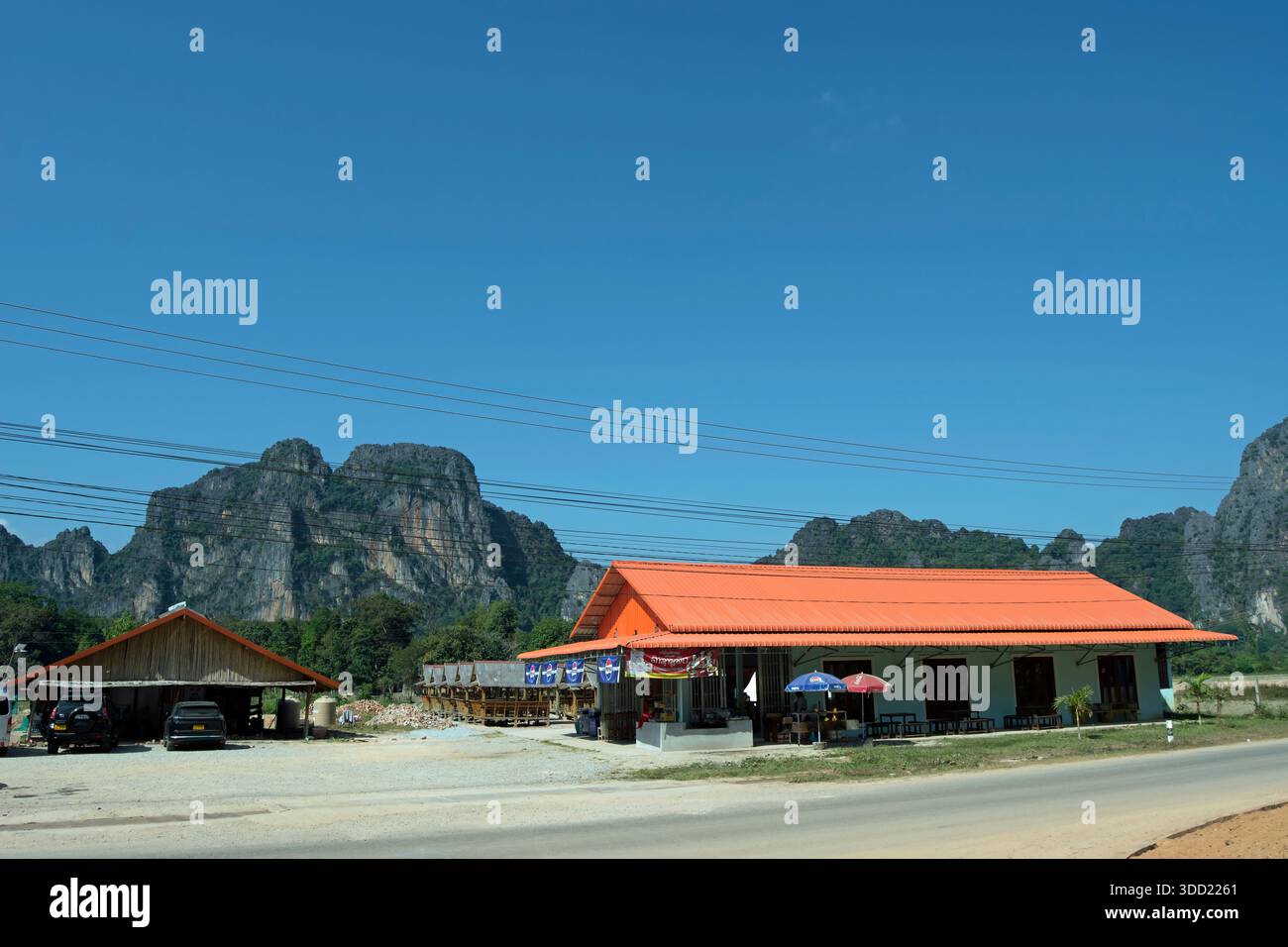 Unter einem blauen Himmel mit Kalksteinkarsten im Hintergrund, ein ruhiges Restaurant am Straßenrand in muang Fuang, laos Stockfoto