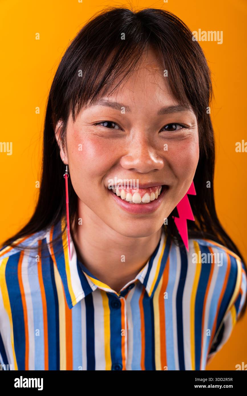 Wunderschönes Porträt einer chinesischen Frau auf farbenfrohem Hintergrund. Asiatische Frau lächelt fröhlich und drückt Freude und Selbstvertrauen aus. Ich trage ein gestreiftes Hemd und pi Stockfoto