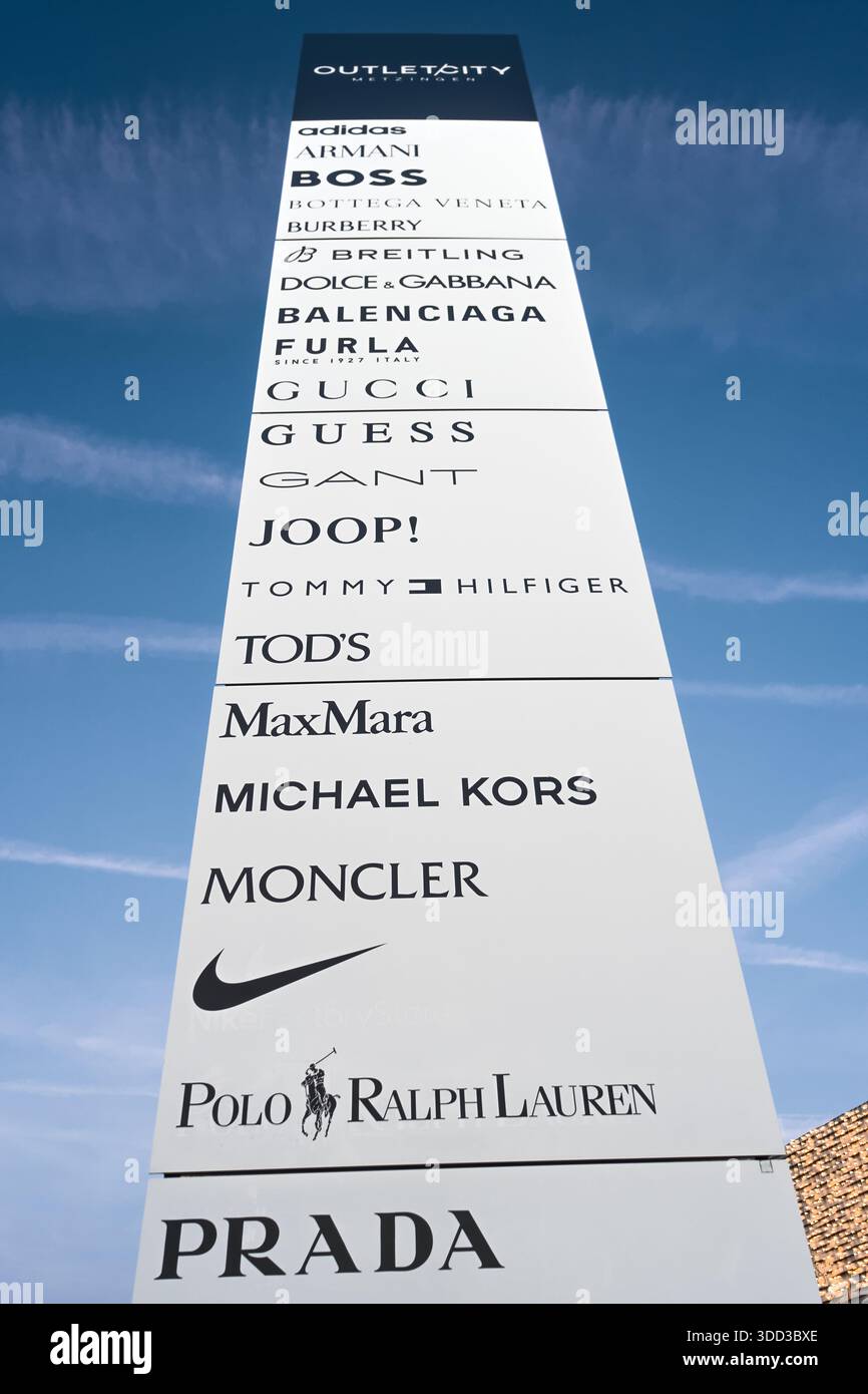 Werbeschild mit mehreren luxuriösen Modenlogos vor klarem blauem Himmel in einem modernen Einkaufsviertel, Outletcity Metzingen Stockfoto