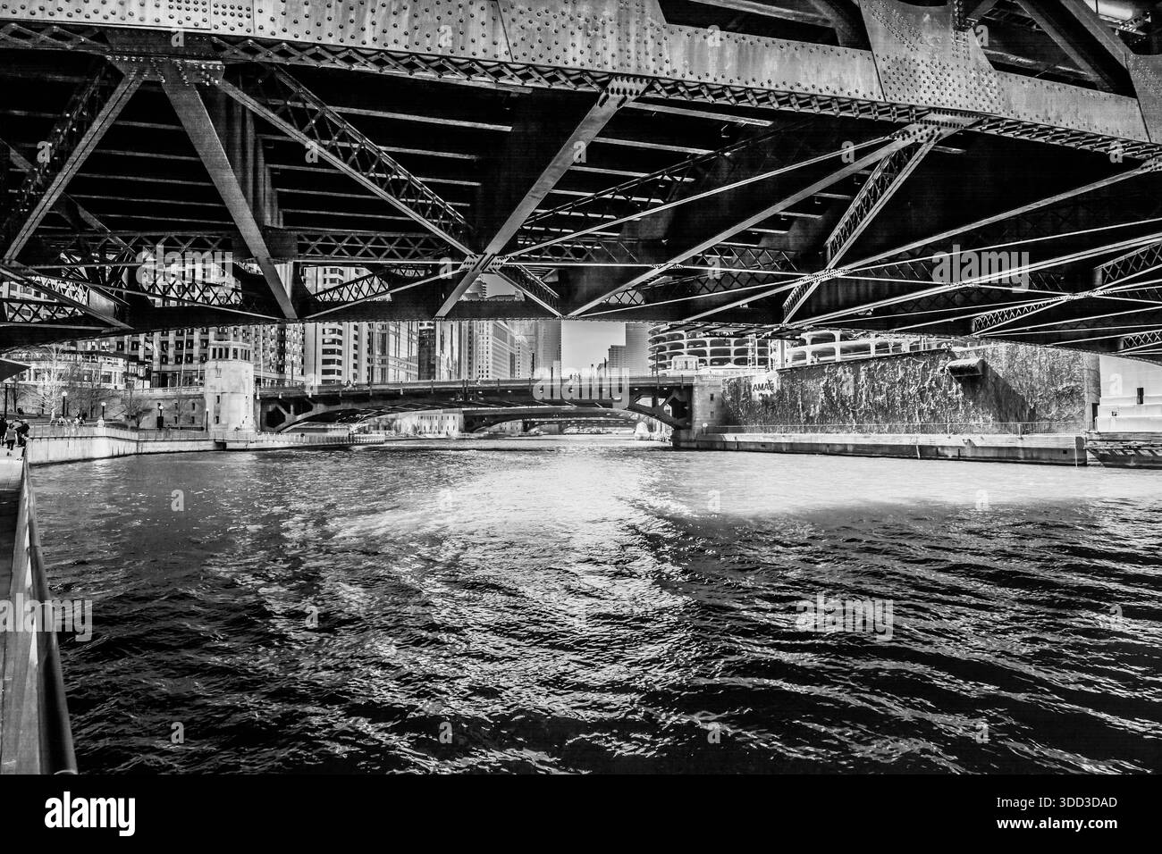 Monochromansicht, die den Chicago River hinunterblickt, eingerahmt vom schweren genieteten Stahlunterbau einer städtischen Klappbrücke. Stockfoto
