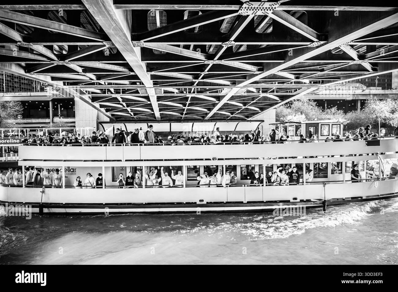 Monochromansicht eines überfüllten Wendella-Tourboots, der unter dem Stahlrahmen einer Klappbrücke auf dem Chicago River vorbeifährt. Stockfoto