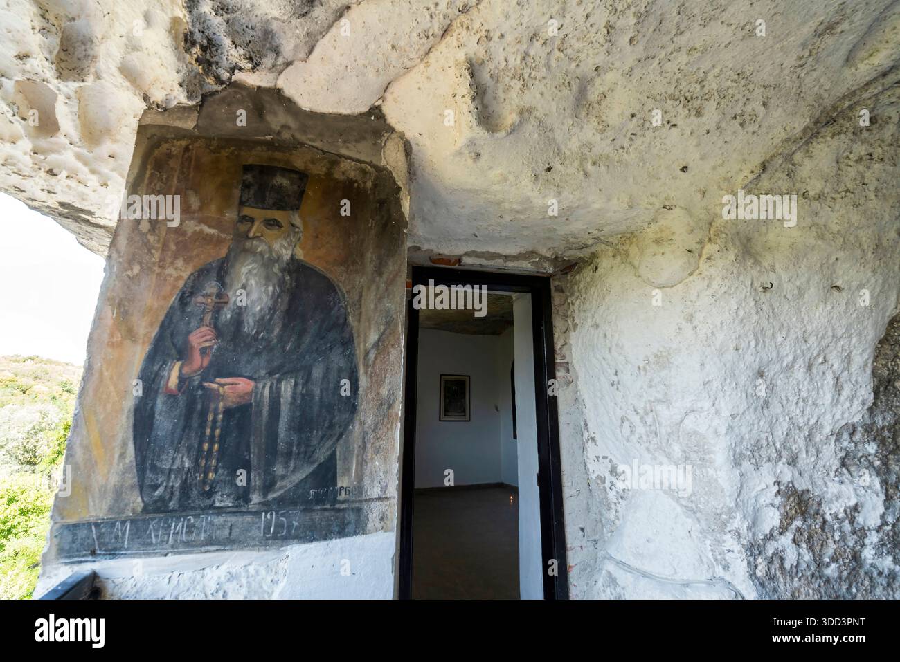 Ein gemaltes Porträt eines bärtigen orthodoxen Mönchs, der ein Kreuz hält, befindet sich am Steineingang des Klosters Basarbovo. Stockfoto