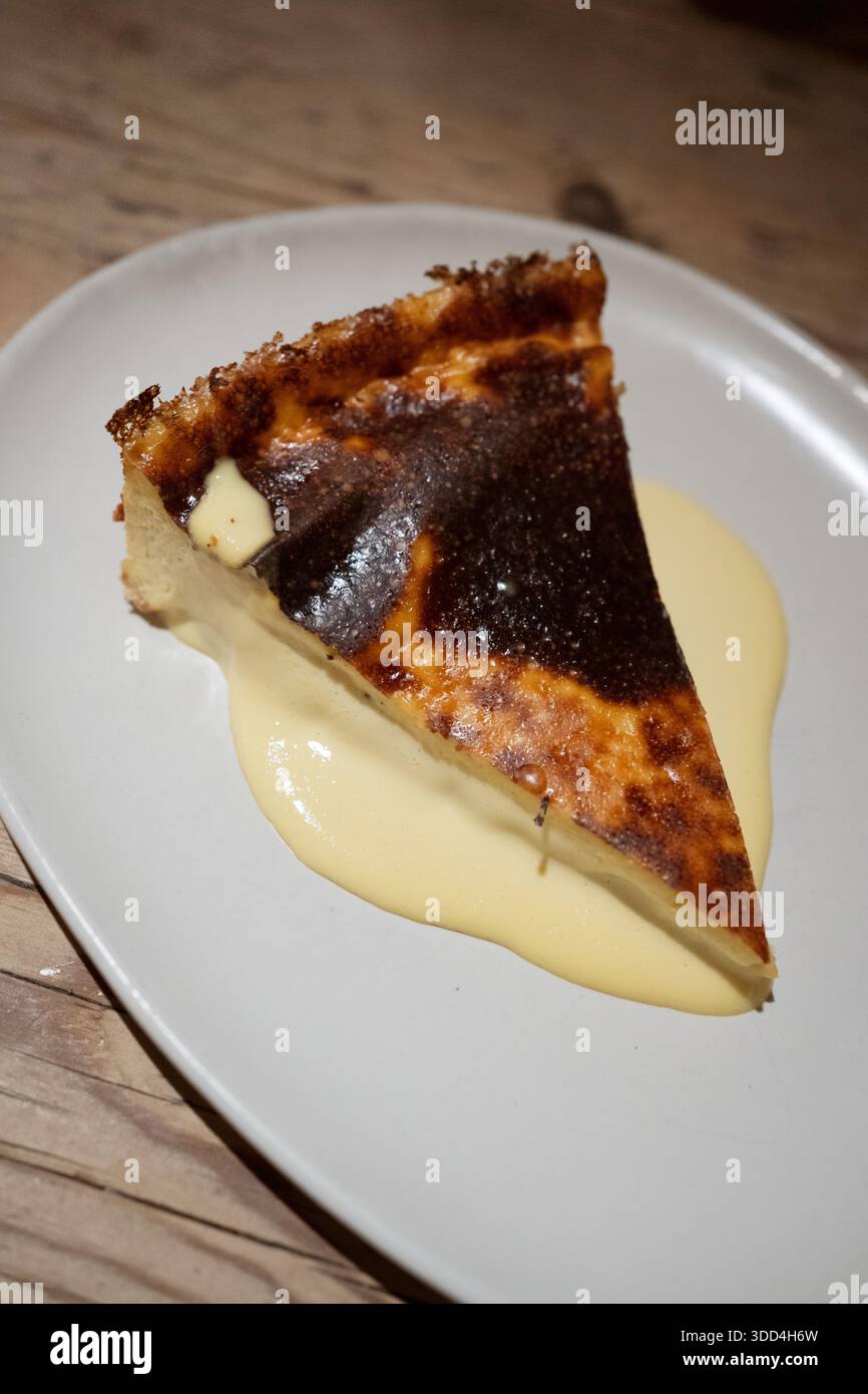 Basque Burnt Cheesecake Scheibe, serviert auf einem weißen Teller mit Vanillesauce Stockfoto
