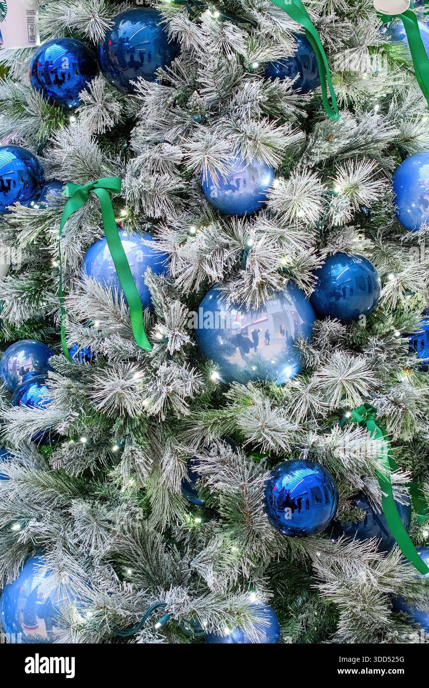 Nahaufnahme eines Weihnachtsbaums mit blauen Ornamenten, grünen Bändern und weißen Lichtern. Stockfoto