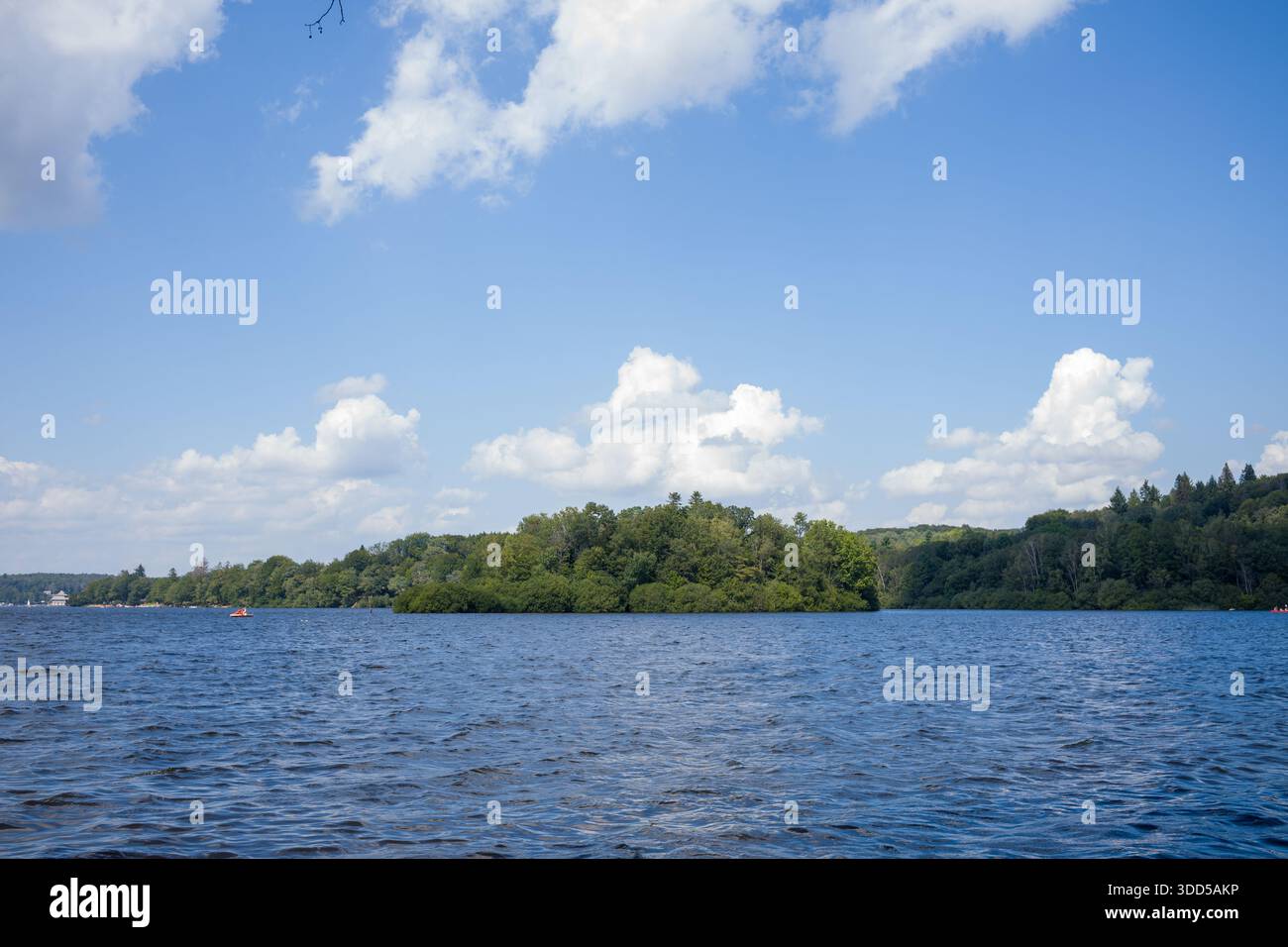 Eine üppig grüne Insel erhebt sich aus dem sanften Wasser des Lac des Settons, umgeben von einem plätschernden blauen See und unter einem Himmel voller geschwollener weißer Wolken. Stockfoto