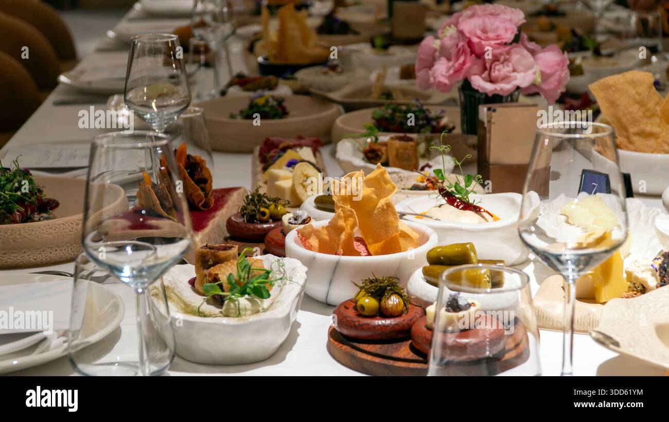 Luxuriöser Banketttisch mit mediterranen Mezze-Vorspeisen, rosafarbenen Mittelstücken und Wein schaffen eine elegante Atmosphäre für eine Veranstaltung Stockfoto