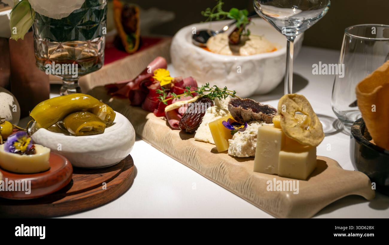 Ein luxuriöses Restaurant mit Wurstaufschnitt, handwerklich hergestellten Käsesorten, Wurstwaren, Datteln und essbaren Blumen wird beim eleganten mediterranen Abendessen serviert Stockfoto