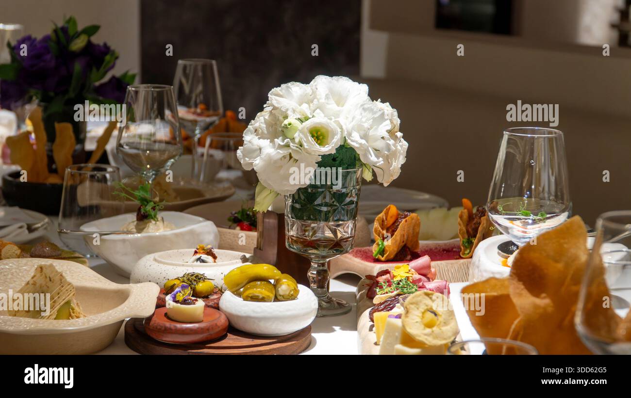 Ein luxuriöses Restaurant mit Wurstaufschnitt, handwerklich hergestellten Käsesorten, Wurstwaren, Datteln und essbaren Blumen wird beim eleganten mediterranen Abendessen serviert Stockfoto