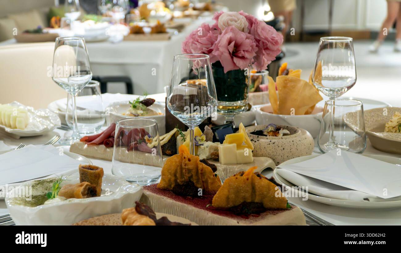 Luxuriöser Restauranttisch mit mediterranen Vorspeisen, rosafarbener Rose und Weingläsern schaffen eine gehobene Atmosphäre Stockfoto
