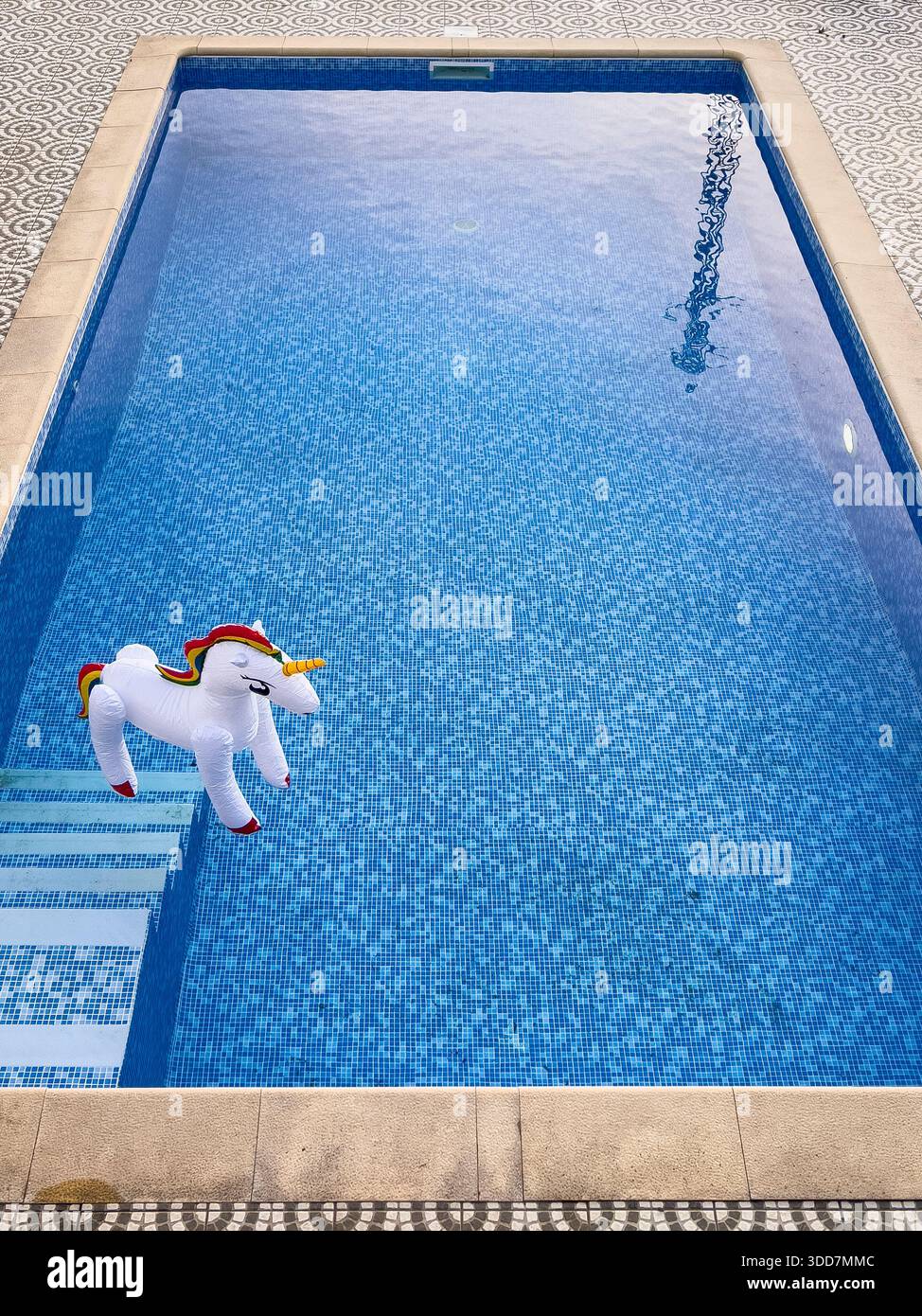 Ein aufblasbares Spielzeug-Einhorn, das in einem Swimmingpool aufrecht auf dem Wasser schwimmt Stockfoto