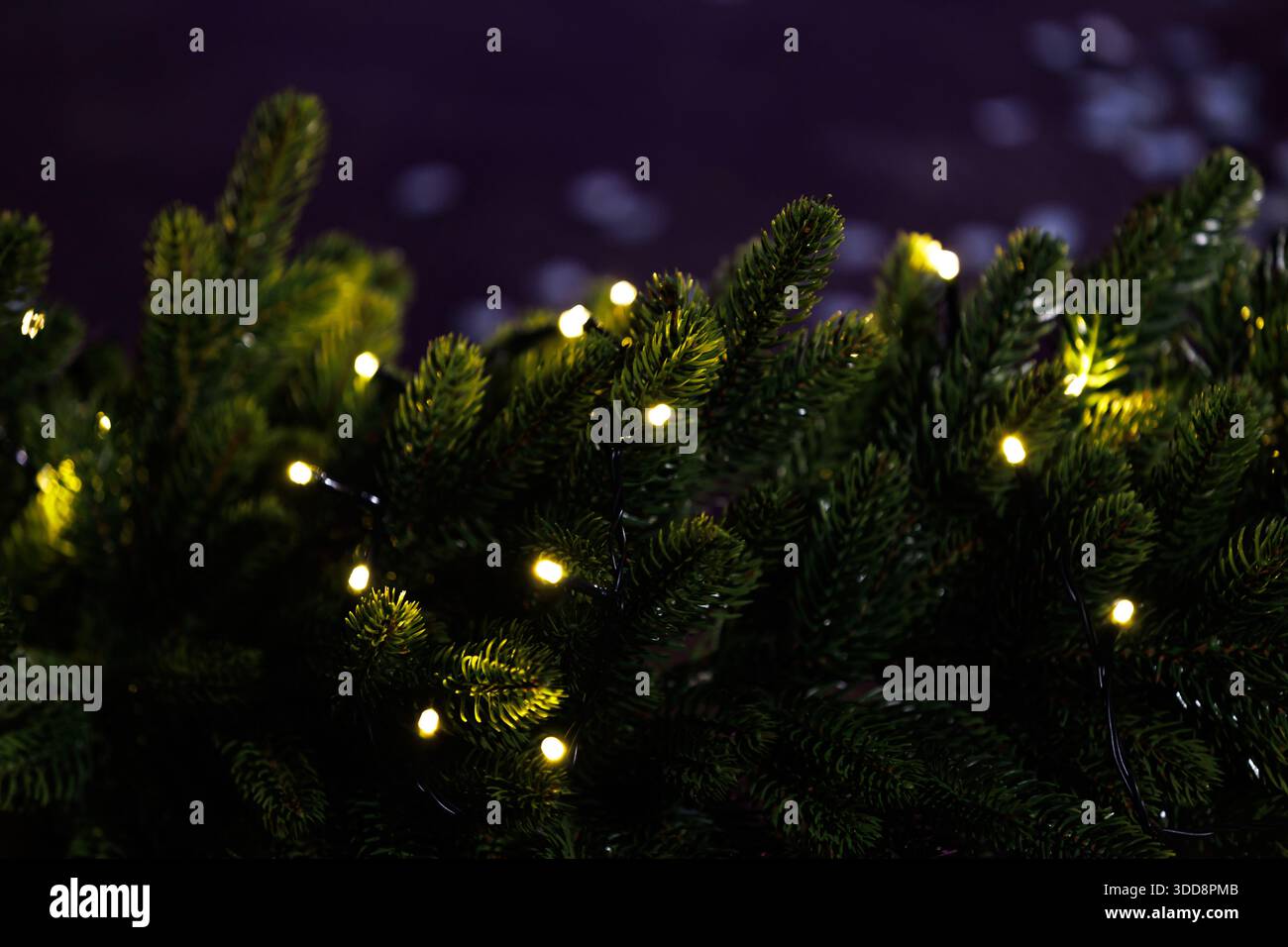Umweltfreundlicher künstlicher Weihnachtsbaum mit warmen Lichtern. Künstlicher Weihnachtsbaum aus recycelten Materialien, dekoriert mit warmen Lichterketten, von Stockfoto