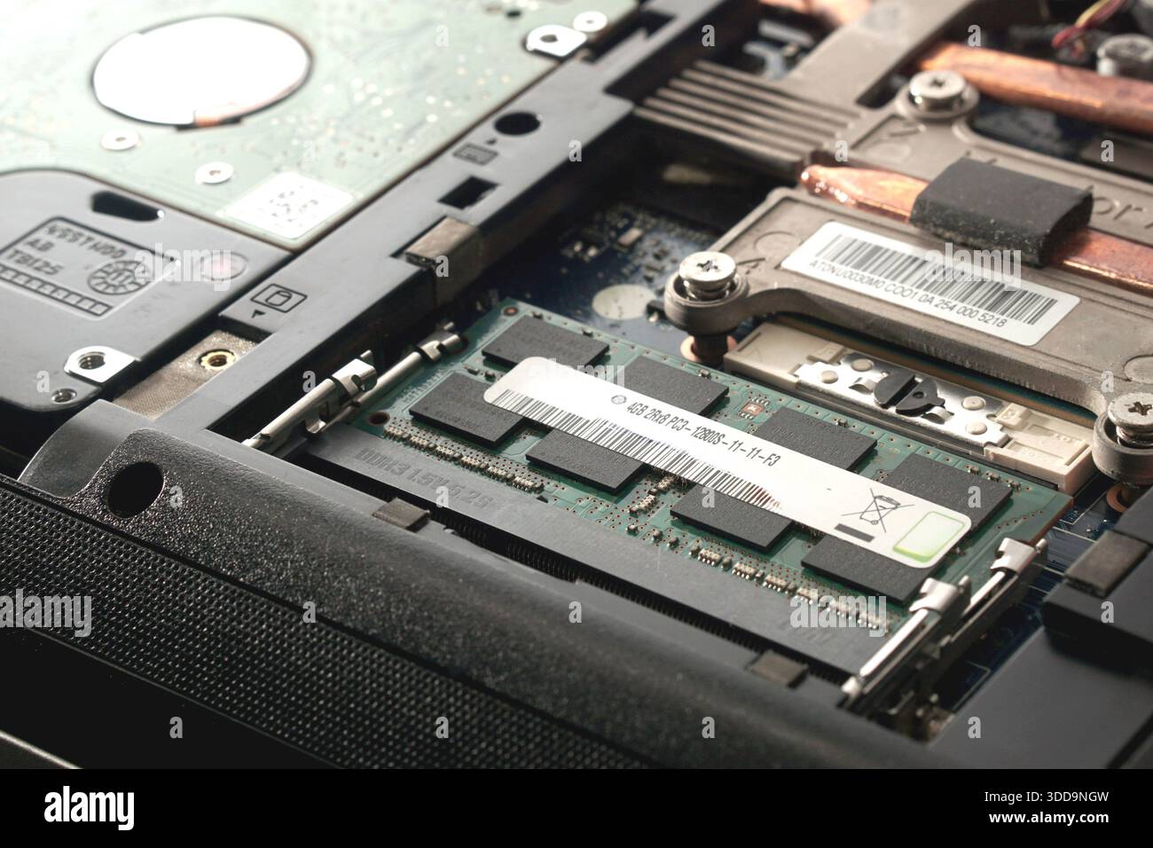 Nahaufnahme eines DDR3-RAM-Moduls, das in einem Laptop-Hauptplatinensteckplatz neben einem Festplattenlaufwerk installiert ist. Stellt Hardwareerweiterung dar, Zweikanal-Konfidenz Stockfoto