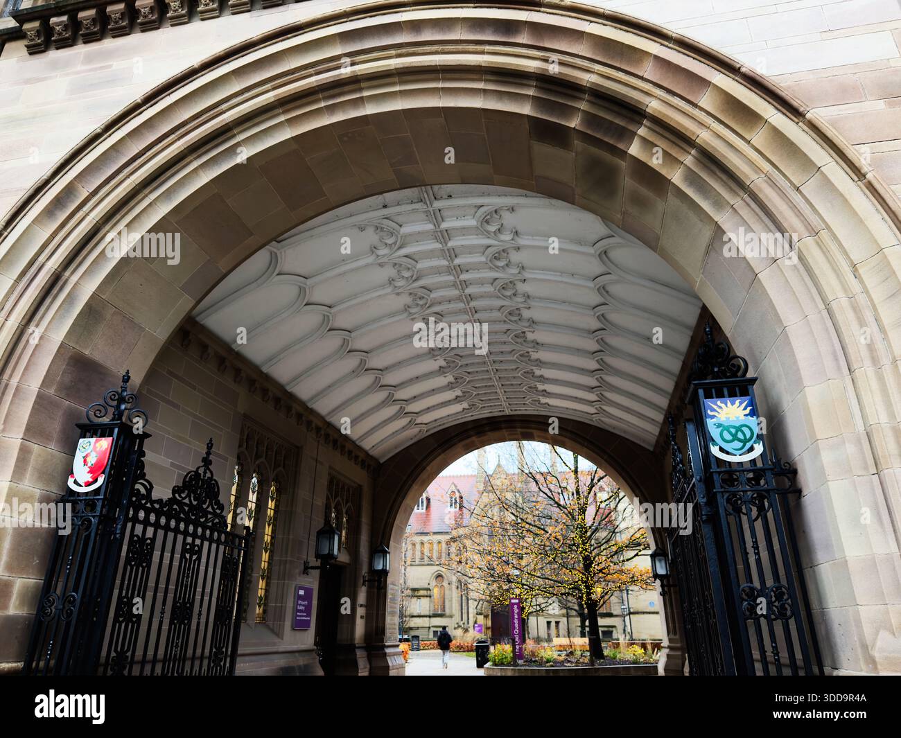 Manchester, Großbritannien - 06. Dezember 2025: Berühmter Torbogen der Universität Manchester mit Wappen, Sandsteintüren und einem mit Bäumen gefüllten Innenhof. Stockfoto
